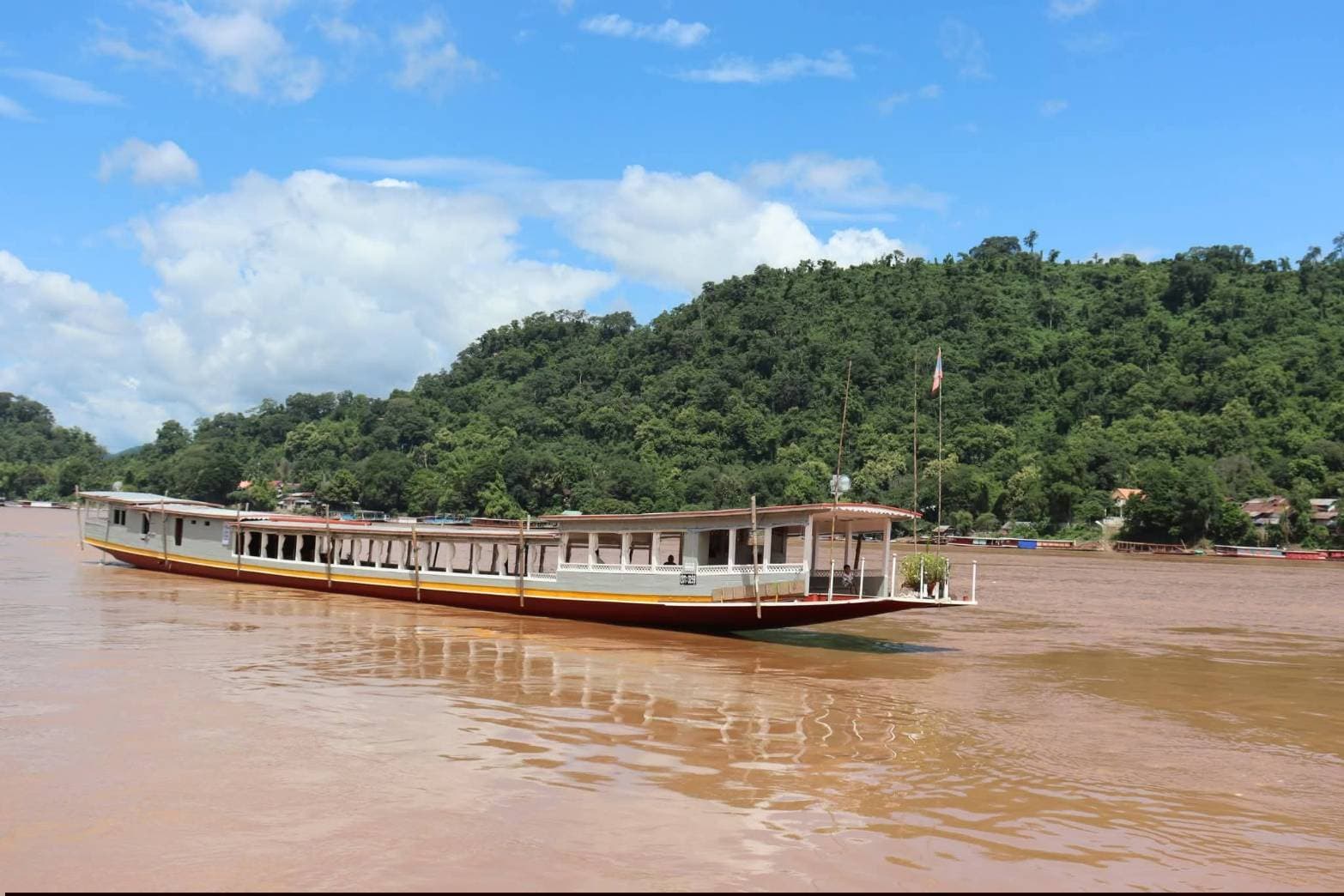 Mekong slow boat with yellow hull on the river below jungle hills