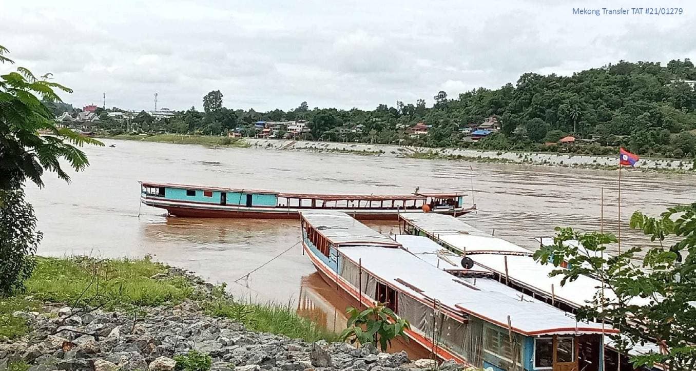 Local slow boats moored at the Mekong pier with a Lao flag